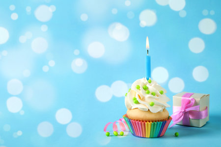 Birthday cupcake with candle and gift box on light blue background, space for text. bokeh effectの写真素材