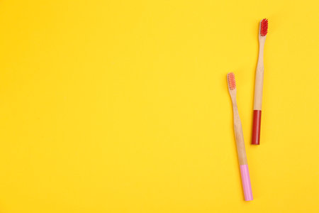 Toothbrushes made of bamboo on yellow background, flat lay. Space for textの写真素材