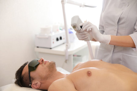 Young man undergoing laser epilation procedure in beauty salonの写真素材
