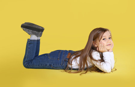 Cute little girl lying on yellow backgroundの写真素材