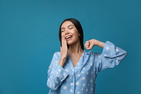 Beautiful Asian woman in pajamas yawning on blue background. Bedtimeの写真素材