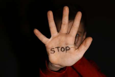 Abused little boy showing palm with word STOP against black background, focus on hand. domestic violence conceptの写真素材