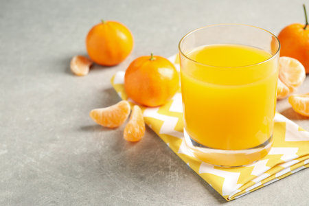 Glass of fresh tangerine juice and fruits on light gray table. Space for textの写真素材