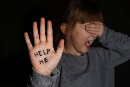 Abused little girl showing palm with phrase HELP ME on black background, focus on hand. domestic violence conceptの写真素材