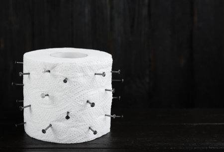 Roll of toilet paper with nails on black wooden table, space for text. Hemorrhoid problemsの写真素材