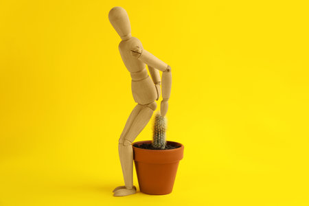 Wooden human figure and cactus on yellow background. Hemorrhoid problemsの写真素材