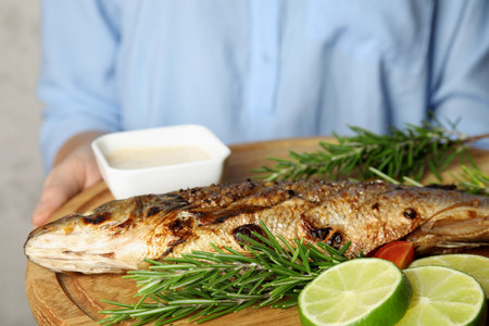 Woman holding wooden board with delicious grilled fish, closeup
