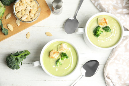 Delicious broccoli cream soup with croutons served on white wooden table, flat layの写真素材