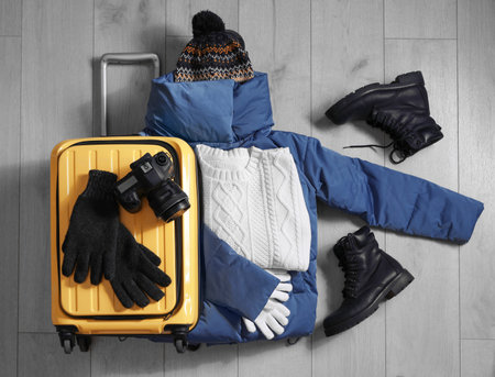 Suitcase with warm clothes and camera on wooden floor, flat lay. winter holidaysの写真素材