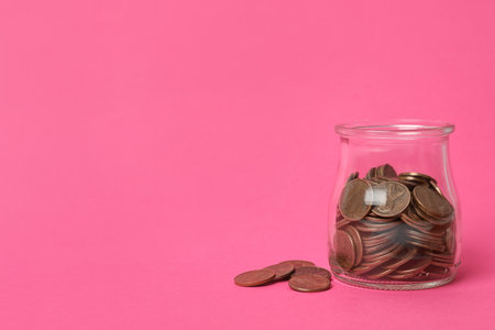 Glass jar with coins on pink background, space for textの写真素材