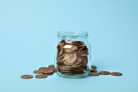 Glass jar with coins on light blue background