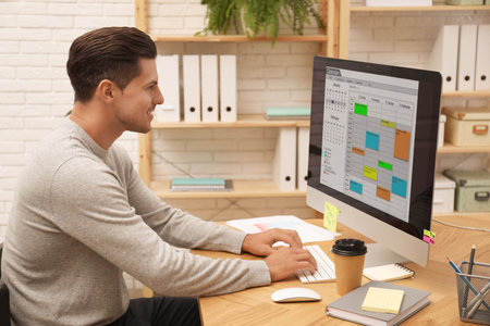 Handsome man using calendar app on computer in officeの写真素材