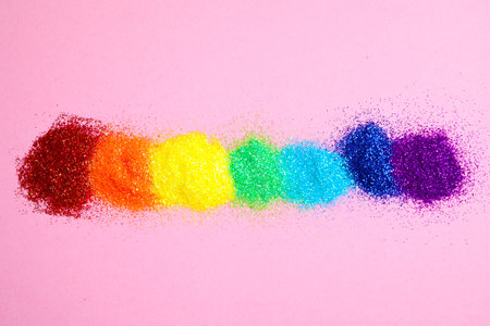 Bright glitters on pink background, flat lay. Rainbow colors