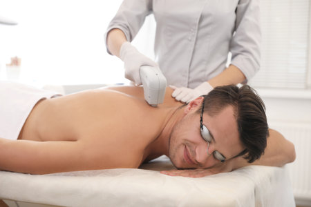 Young man undergoing laser epilation procedure in beauty salonの写真素材