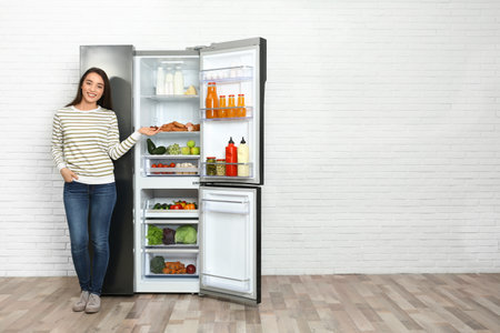 Happy young woman near open refrigerator indoors, space for textの写真素材