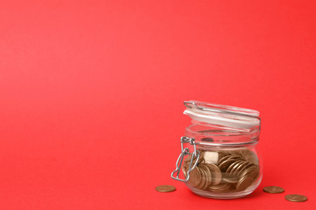 Glass jar with coins on red background, space for textの写真素材