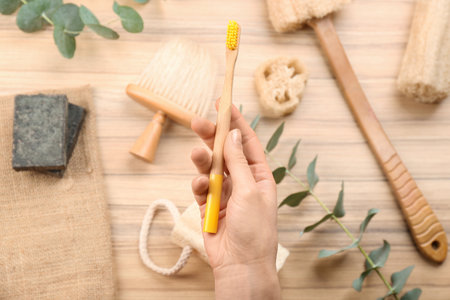 Woman holding natural bamboo toothbrush over table with bath items, top viewの写真素材