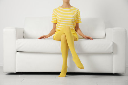 Woman wearing yellow tights sitting on sofa indoors, closeupの写真素材