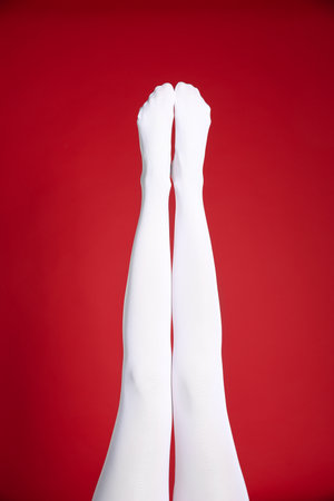 Woman wearing white tights on red background, closeup of legsの写真素材