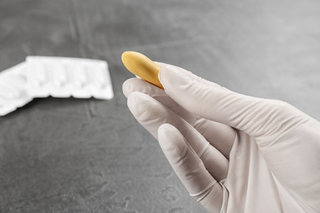 Woman holding suppository at gray table, closeup. Hemorrhoid treatment