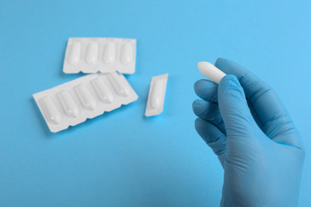Woman holding suppository on light blue background, closeup. Hemorrhoid treatment