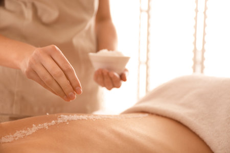 Young woman having body scrubbing procedure with sea salt in spa salon, closeupの写真素材