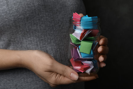Woman holding glass jar with colorful paper pieces, closeup on handsの写真素材