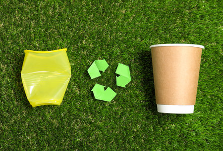 Recycling symbol, plastic and paper cups on green grass, flat layの写真素材