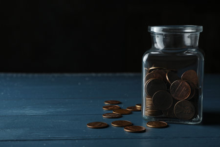 Glass jar with coins on blue wooden table, space for text