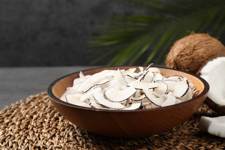 Tasty coconut chips in bowl on wicker mat