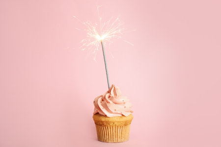 Birthday cupcake with sparkler on pink backgroundの写真素材