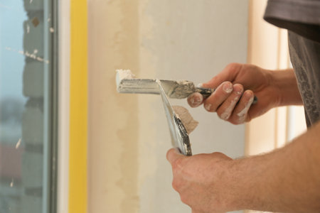 Professional worker with putty knives and plaster near window indoors, closeup. interior repairの写真素材