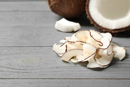 Pile of tasty coconut chips on gray wooden table. Space for text