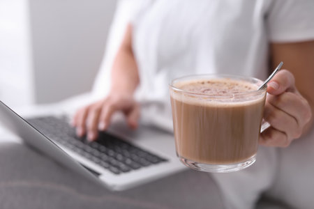 Woman with cup of morning coffee working on laptop indoors, closeupの写真素材