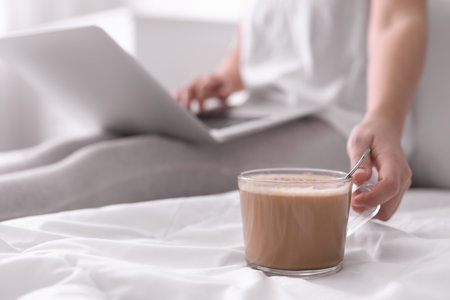 Woman taking cup of morning coffee while working on laptop in bedroom, closeupの写真素材