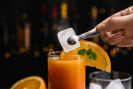 Bartender putting ice cube into glass with Tequila Sunrise cocktail, closeupの写真素材