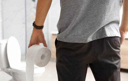 Man with paper roll near toilet bowl in bathroom, closeupの写真素材