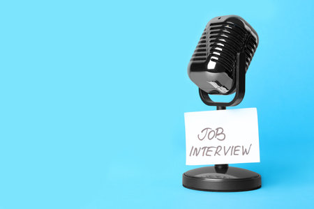 Retro microphone and reminder note with words JOB INTERVIEW on light blue background, space for textの写真素材