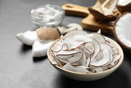 Tasty coconut chips in bowl on black table