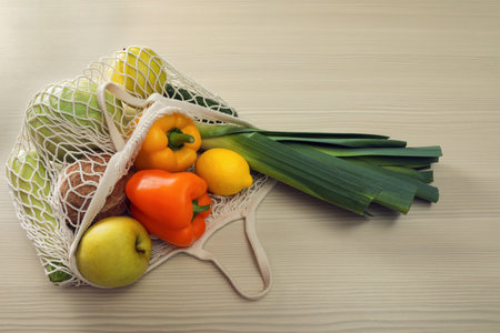 Net bag with vegetables and fruits on wooden table