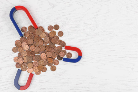 Magnets attracting coins on white wooden table, flat lay. Space for text