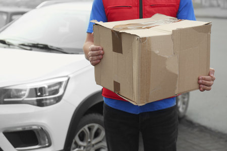 Courier with damaged cardboard box outdoors, closeup. Poor quality delivery serviceの写真素材