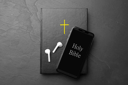 Bible, phone and earphones on black background, top view. religious audiobook