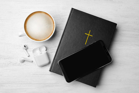 Bible, phone, cup of coffee and earphones on white wooden background, flat lay. religious audiobookの写真素材