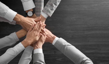 People holding hands together over gray wooden background, top view. unity concept