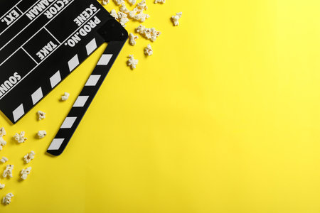 Clapper board and popcorn on yellow background, flat lay with space for text. Visiting cinemaの写真素材