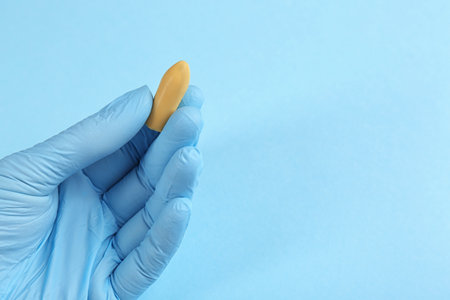 Closeup view of woman holding suppository on light blue background, space for text. Hemorrhoid treatmentの写真素材