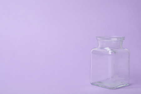 Open empty glass jar on lilac background, space for textの写真素材