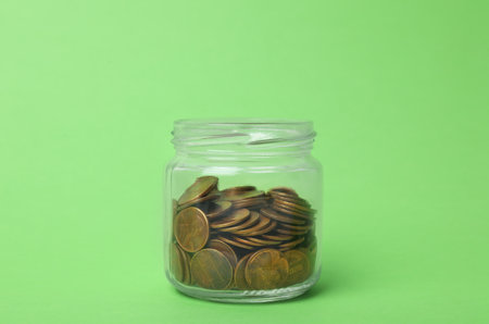 Glass jar with coins on light green background