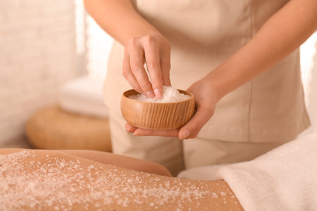 Young woman having body scrubbing procedure with sea salt in spa salon, closeupの写真素材